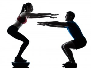 Personal trainer doing a squat with his female client doing one too