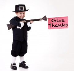 Child dressed as a pilgrim with a sign that says "give thanks"
